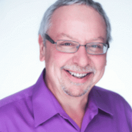 Smiling male professor, with short-cropped grey hair and a grey goatee, wearing glasses and a violet collared shirt
